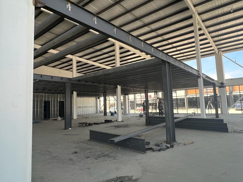 Estructura de un edificio comercial con vigas y columnas de acero oscuro que sostiene el entrepiso, techo de acero inoxidable en la bodega de Kelder Zertuche Ensenada.