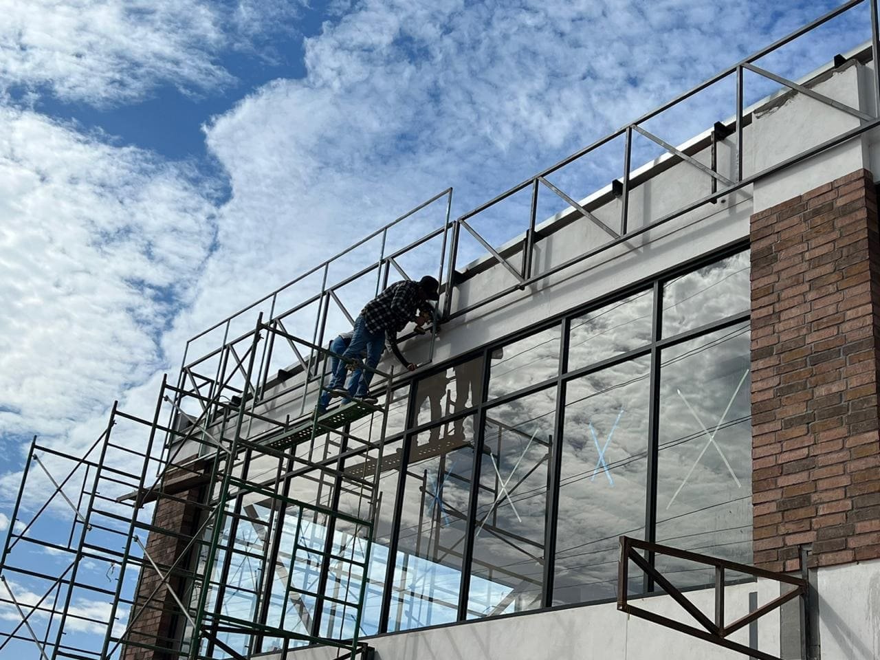 Dos hombres arriba de un andamio trabajando en la frachada estructural de construcción de bodega comercial en Kelder Zertuche Ensenada