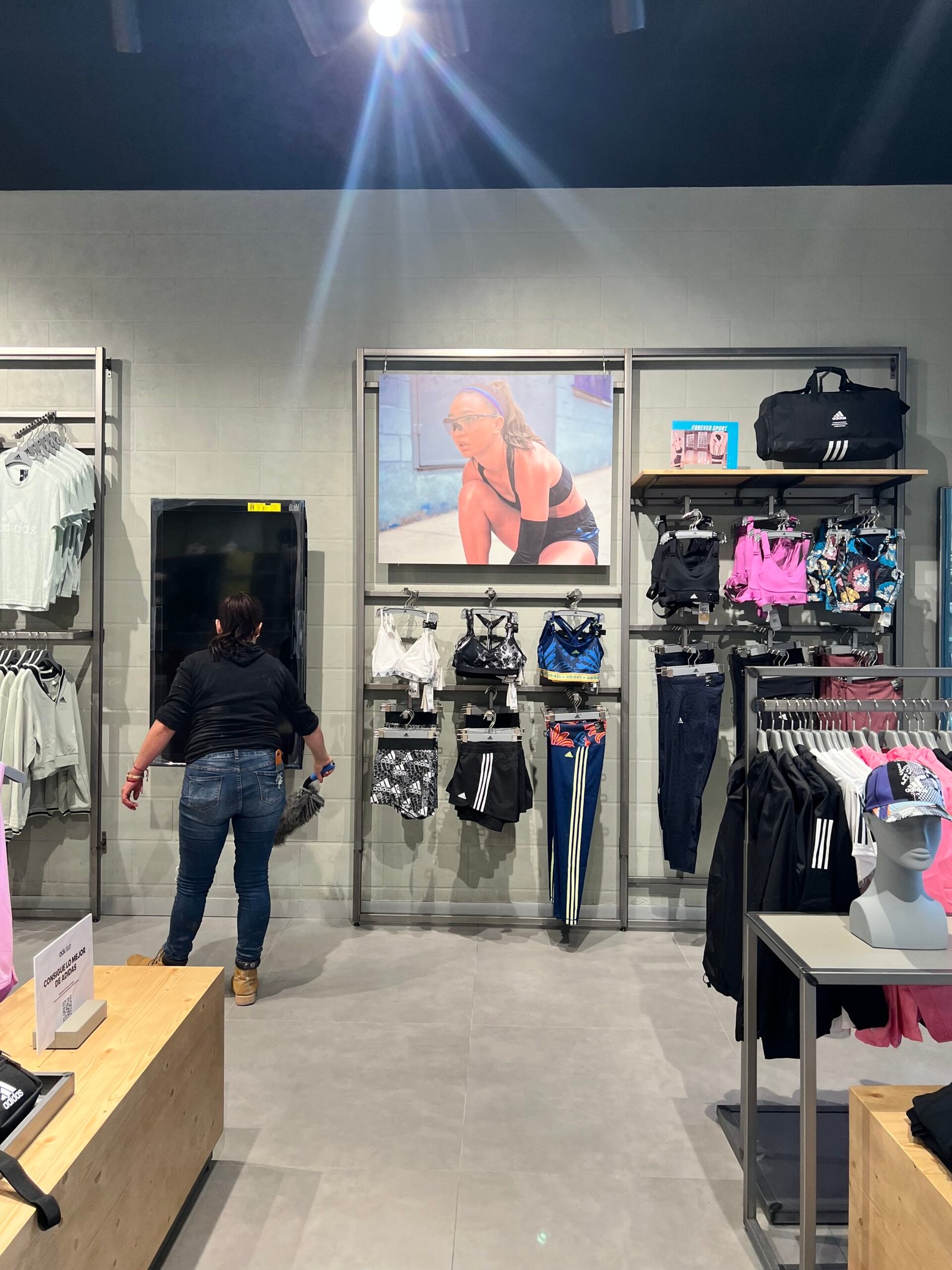 mujer de espaldas frente a un muro de block aparente dentro de una tienda comercial de ropa deportiva