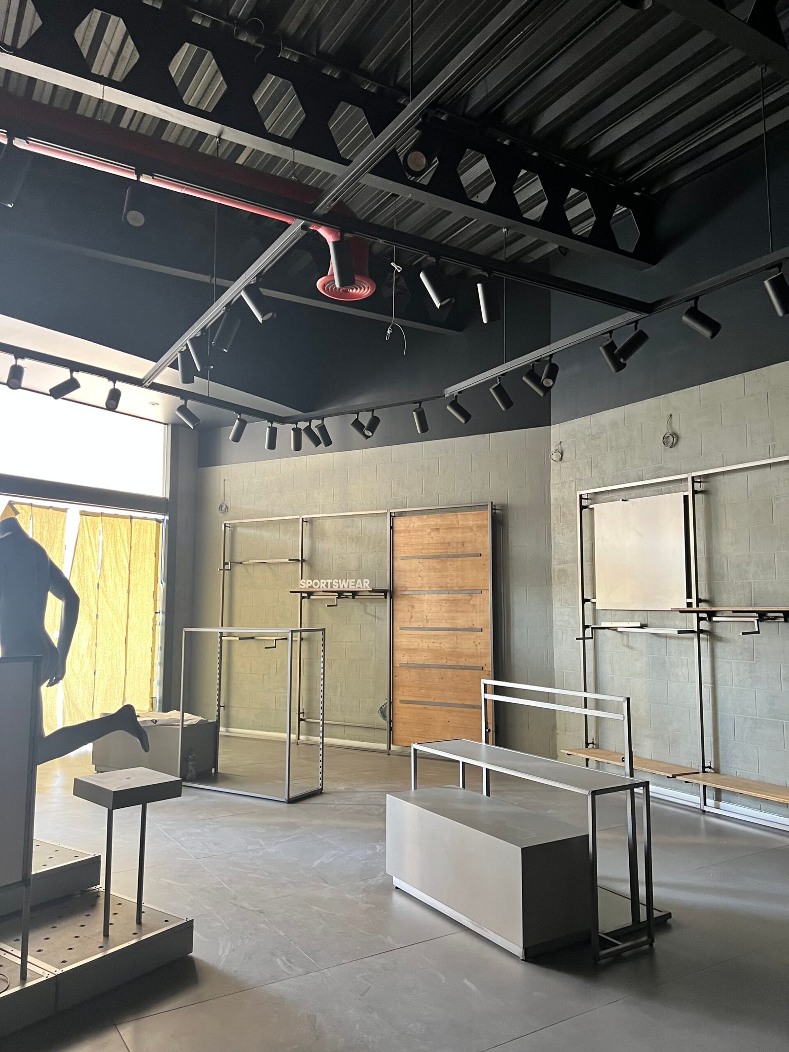 Interior de local comercial en fase de equipamiento con mobiliario de exhibición metálico, muros de block aparentes pintados y techo industrial con rieles de iluminación.