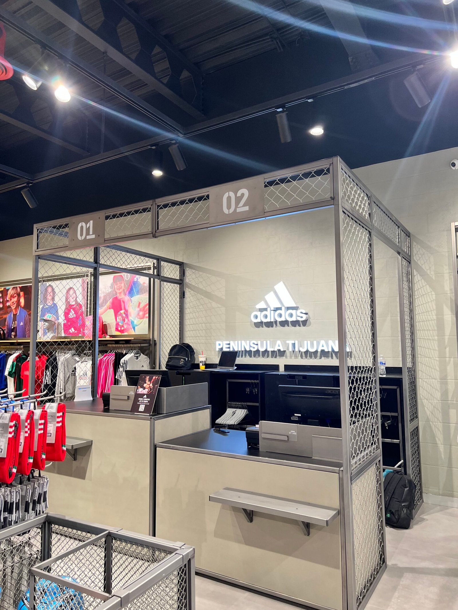 Vista de un mostrador de cobro de diseño industrial en una tienda Adidas, construido con una estructura de metal galvanizado y paneles de malla de alambre.