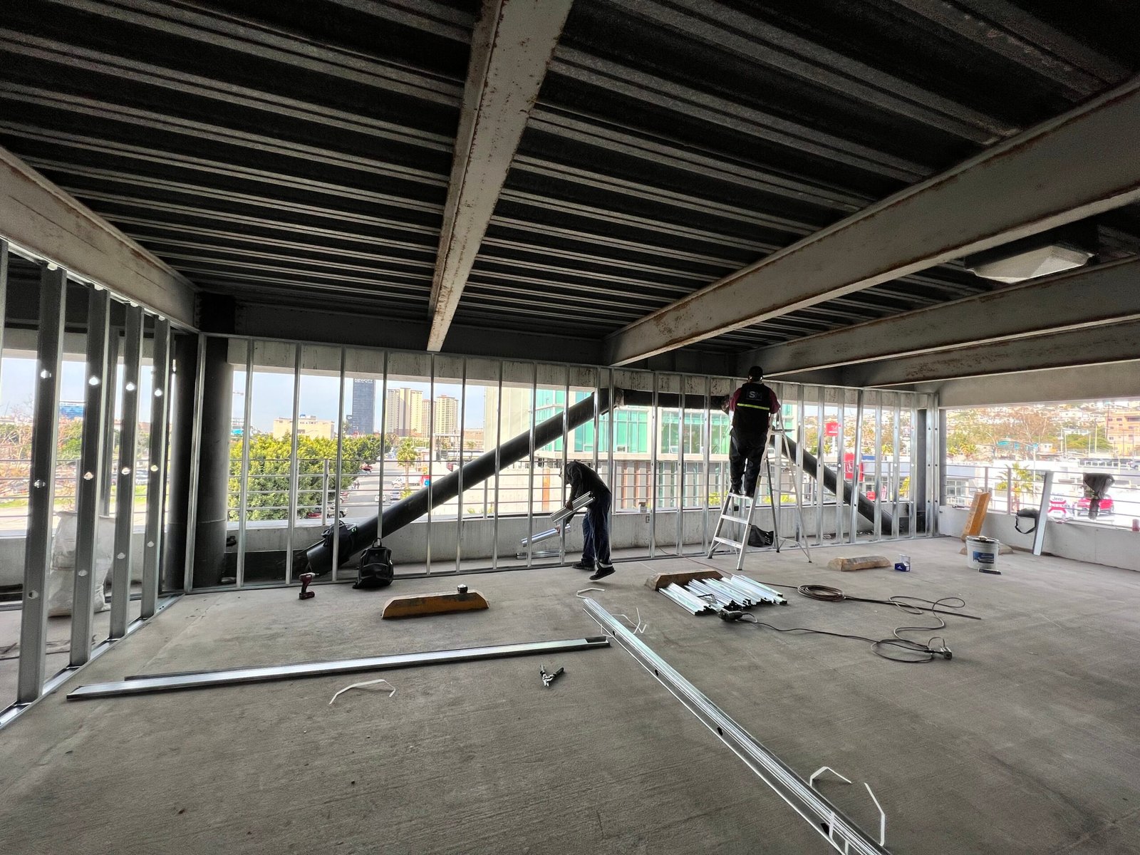 Hombre arriba de una escalera instalando postes metálicos en ampliación en Mercedes Benz tijuana
