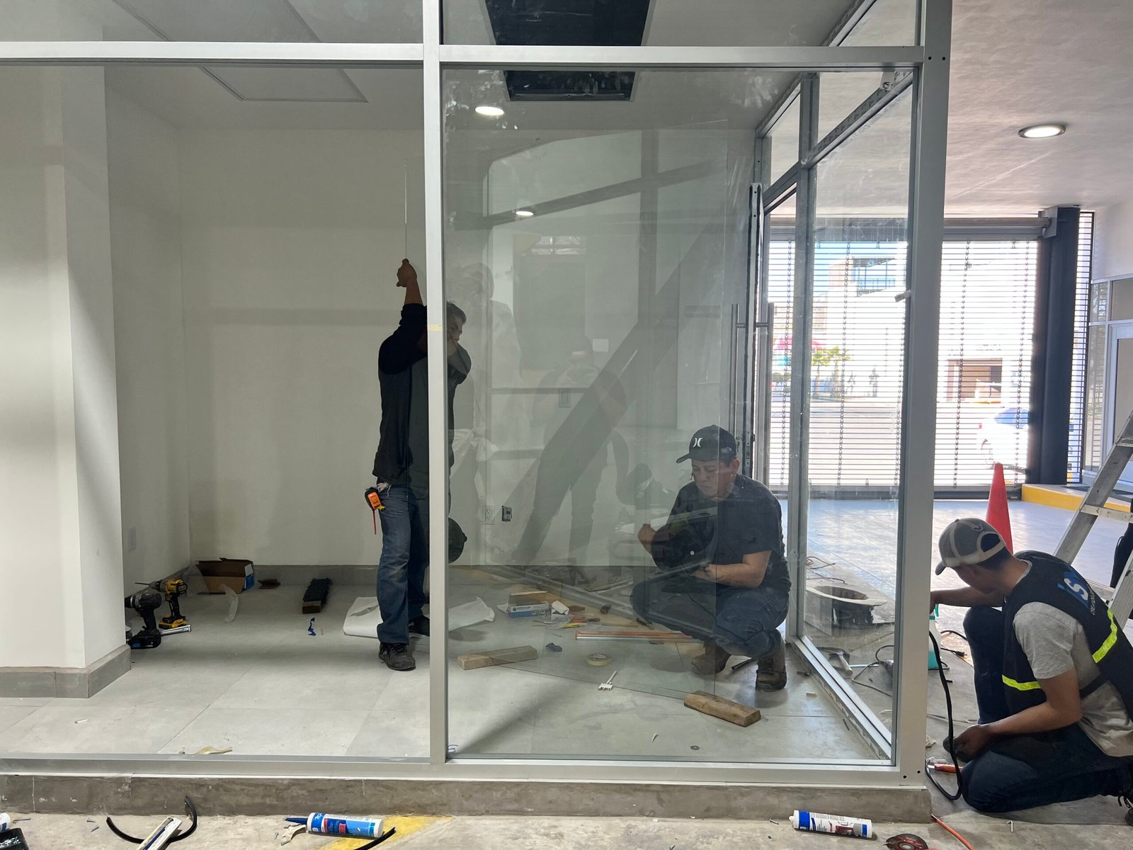 3 hombres trabajando en la instalación de cancelería de vidrio templado en oficina de Mercedes Benz en Tijuana
