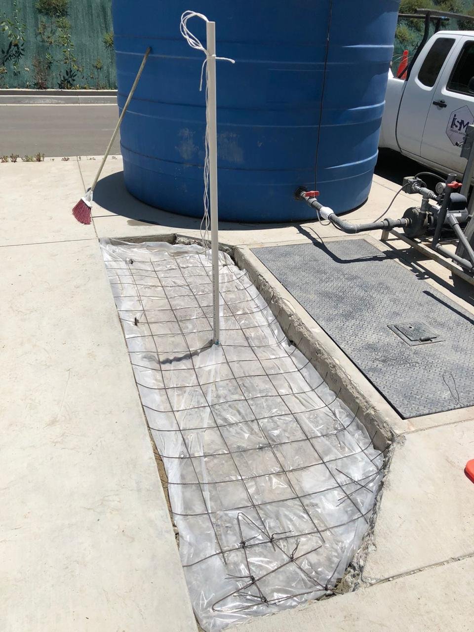 Preparación de terreno con plástico y malla electrosoldada para colado de concreto, ubicada junto a una cisterna de agua azul, tuberías conectadas a una bomba hidráulica, en proyecto de sistema hidrico en tijuana